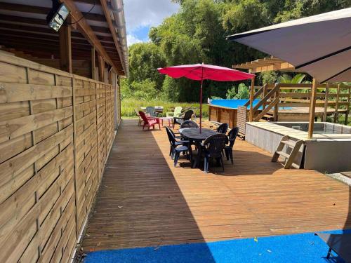 a wooden deck with tables and chairs and a red umbrella at Le Pavillon Ananas in Gros-Morne
