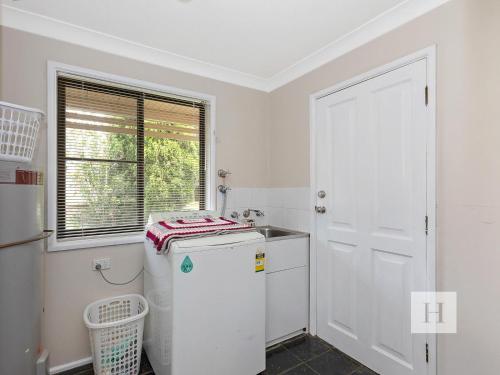 a white kitchen with a refrigerator and a window at Mannering Lake House in Mannering Park