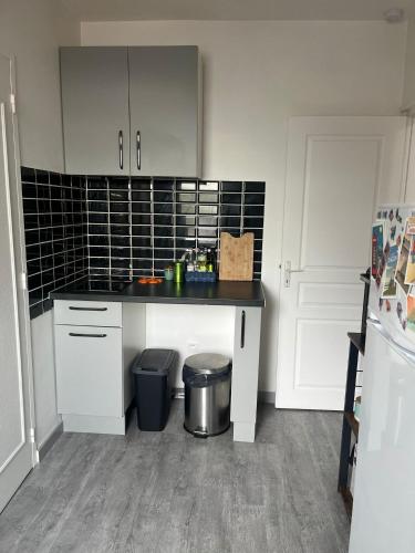 d'une cuisine avec des placards blancs et un mur en carrelage noir. dans l'établissement Appartement T2 Montargis, à Montargis