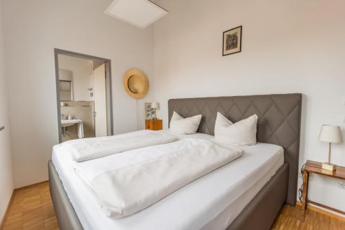 a white bedroom with a large bed with white sheets at Hotel Freischütz Apartments in Landshut