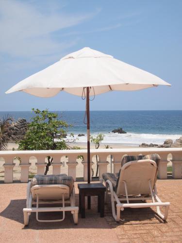 two chairs and a table with an umbrella next to the beach at Hotel Santa Fe in Puerto Escondido