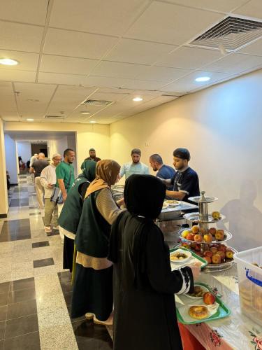 eine Gruppe von Menschen steht mit Essen um einen Tisch herum in der Unterkunft فندق نوم وسكون in An Nikāshah