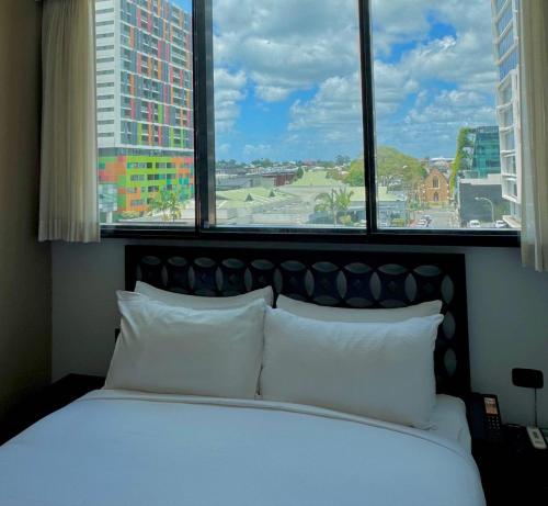 a bed with white pillows in a room with windows at The Constance Fortitude Valley in Brisbane