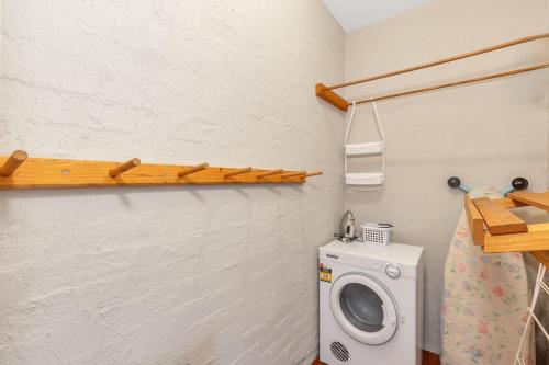 a laundry room with a washing machine and a shelf at Snowbird 1 - Charming 2BR Townhouse l Lake Views l Air-Con l Off-Street Parking in Jindabyne