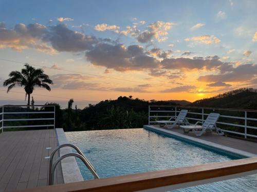 a swimming pool with two chairs and a sunset at Casa Kairos CR, Playa Samara in Nicoya