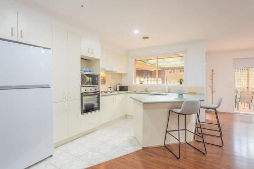 una cucina con armadi bianchi e 2 sgabelli di Well-Appointed Family Home in Popular Location a Tarneit