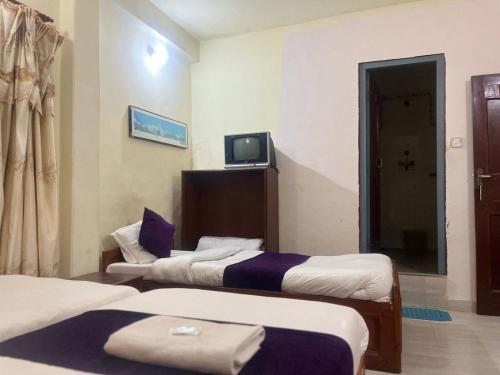 a room with two beds and a tv on the wall at Hotel Blue lake in Pokhara