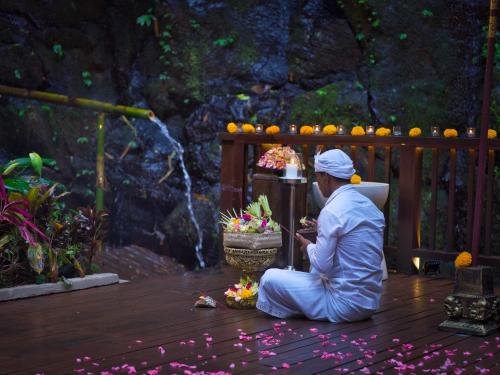 a man in white sitting on a deck with a pot of flowers at Nandini Jungle by Hanging Gardens in Payangan