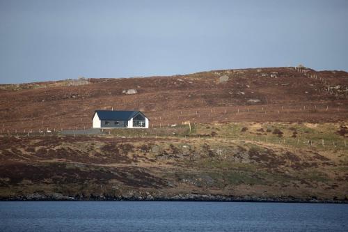 a house on top of a hill next to the water at Modern and Dog Friendly Holiday Home with Sea Loch Views in Breaclete