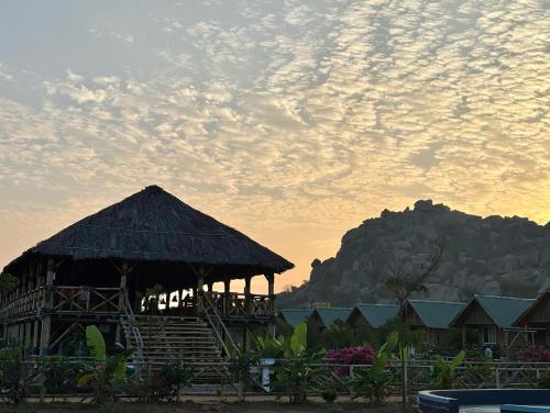 a resort with a thatched building with a mountain in the background at Mowgli's Cafe Hampi & Guest House in Hampi