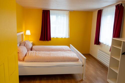 a yellow bedroom with a bed and two windows at Schlafen zur Brauerei St. Johann in Nesslau