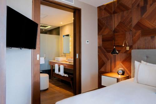 a bedroom with a bed and a bathroom with a sink at The Fives Downtown Hotel & Residences, Curio Collection by Hilton in Playa del Carmen