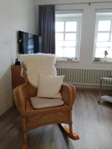 a wicker rocking chair with a pillow in a living room at Hotel Garni Friesenhuus in Greetsiel