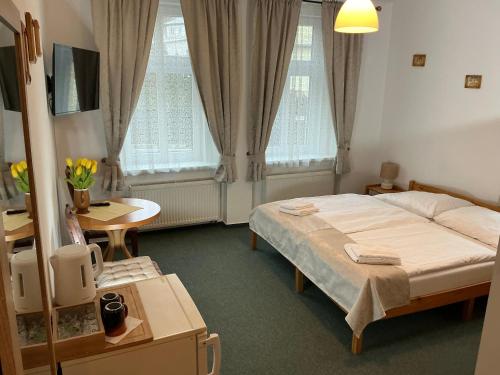 a bedroom with a bed and a table and two windows at Pension Abbazia in Františkovy Lázně