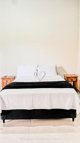 a bed with a black and white blanket and two tables at Pousada Emerências dos Búzios in Armacao dos Buzios