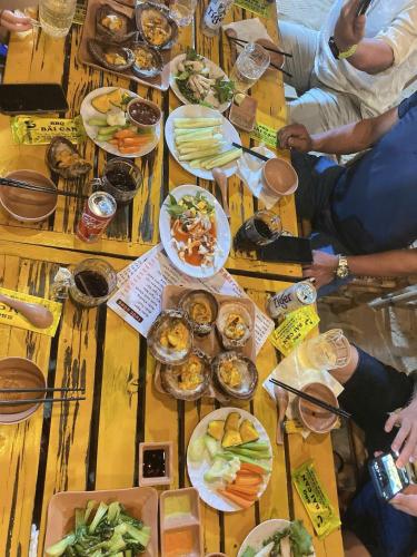 a group of people sitting around a wooden table with food at Homestay Hoàng Phúc in Cu Lao Thu