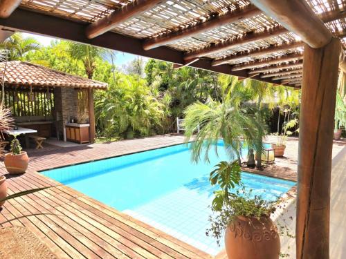 a swimming pool with a pergola and a house at Chalé Carnaval do Sol, Arraial d'Ajuda in Porto Seguro