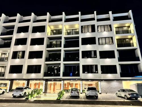 a large white building with cars parked in a parking lot at Medad Apartments Al Hamra in Al Khobar
