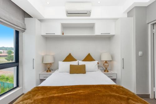 a white bedroom with a large bed with two lamps at The Regency Apartments in Pretoria
