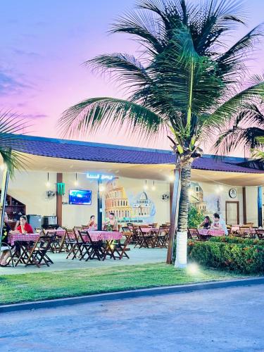a group of people sitting outside of a restaurant with a palm tree at Hotel & Pousada Italia Beach - Porto Das Dunas in Aquiraz