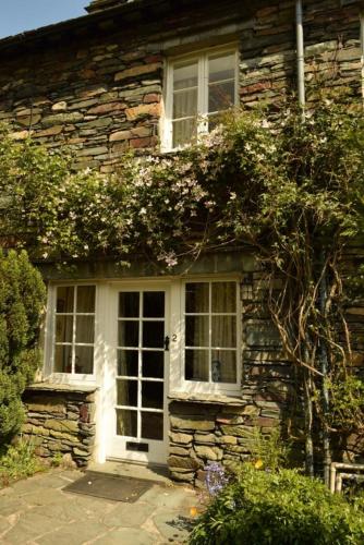 a stone house with a white door and windows at 2 Bridge Syke, Elterwater in Chapel Stile