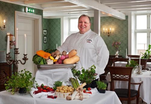 a chef standing in front of a table with vegetables at Hotel Kong Carl - Unike Hoteller in Sandefjord