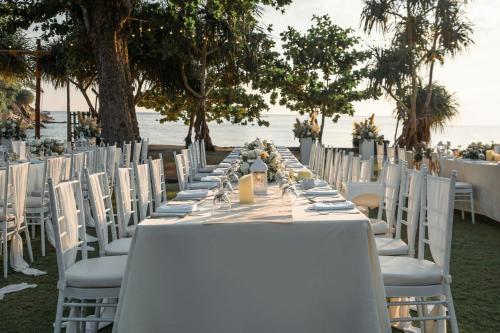 a long dining table with white chairs and a beach at Phuket Marriott Resort & Spa, Merlin Beach in Patong Beach