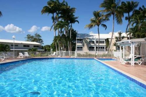 a large blue swimming pool with palm trees and a building at Superbe studio avec Piscine, au coeur de la Marina! Village Soleil ! Proche Aéroport & Ferry in Le Gosier