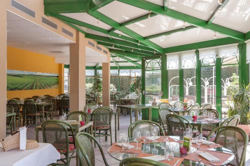 a restaurant with green ceilings and tables and chairs at LOGIS Hotel l'Escargotière Dijon Sud - Chenove in Chenôve