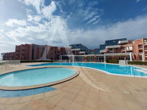 une grande piscine avec des bâtiments en arrière-plan dans l'établissement studio vue mer parking piscine tennis, à Sète