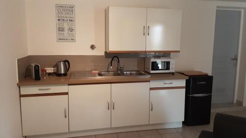 une cuisine avec des armoires blanches, un évier et un micro-ondes dans l'établissement Les acacias, à Gréoux-les-Bains