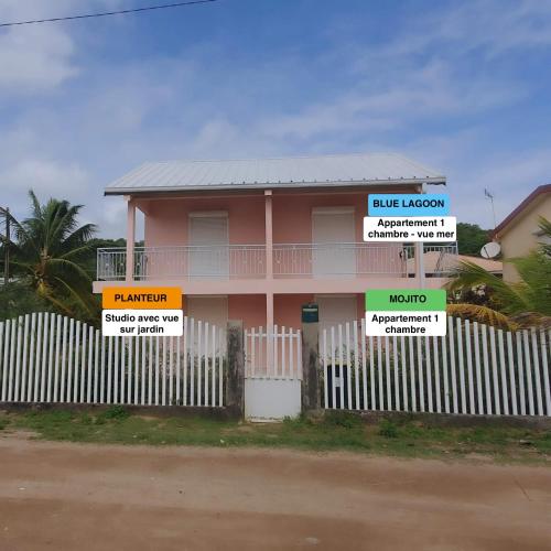 a pink house behind a fence with signs on it at Kozy Kaz - Les pieds dans l eau in La Trinité