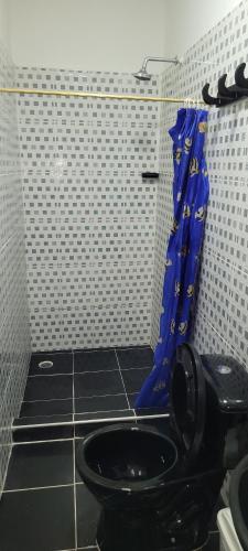 a bathroom with a black toilet with a blue shower curtain at Hostal Villa del Río Las Brisas in Villavieja