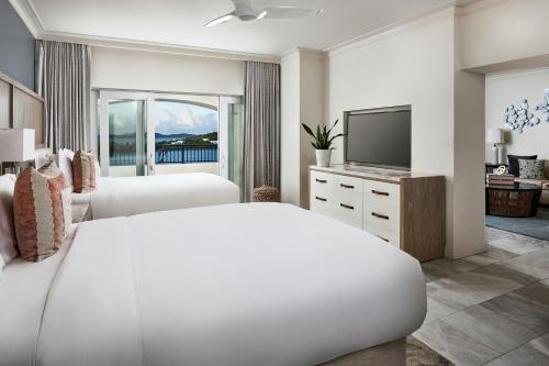 a white bedroom with two beds and a television at The Ritz-Carlton St. Thomas in Benner