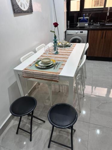 a white table with two black chairs and a kitchen at Elegant & Contemporary Stay in Temara