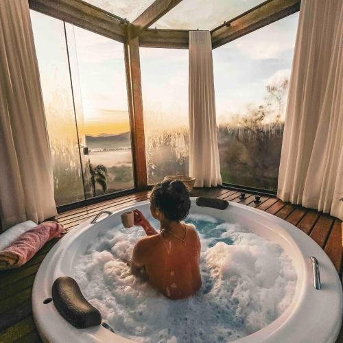 a man sitting in a bath tub in front of a window at Refúgio Terras Altas in Itanhandu