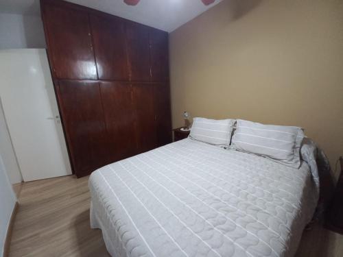 a bedroom with a bed with white sheets and a wooden cabinet at Magnífica casa con cochera privada in Luján