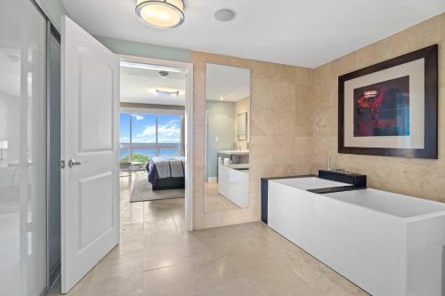 La salle de bains est pourvue d'une grande baignoire blanche et d'un miroir. dans l'établissement Beachfront - Panoramic View 4BR Penthouse - PH4, à Palm-Eagle Beach