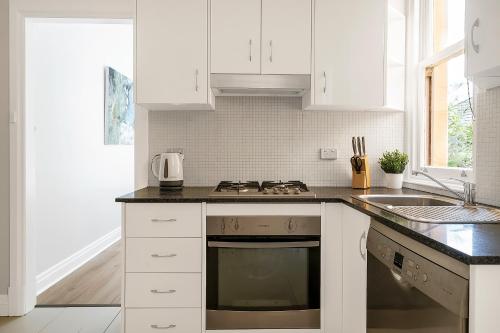 a white kitchen with a stove and a sink at Renovated Harbourfront Home With Harbour Views in Sydney