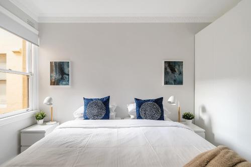 a white bedroom with a large bed with blue pillows at Renovated Harbourfront Home With Harbour Views in Sydney