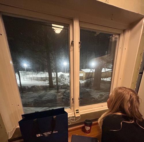 a woman sitting in front of a window at night at Vasaloppsgården - egen hockeyrink in Evertsberg