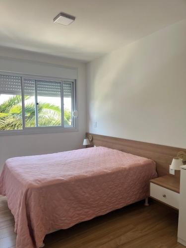 a bedroom with a bed with a pink bedspread and a window at Apartamento alto padrão in Xangri-lá
