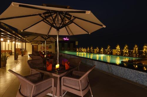 a table with an umbrella next to a swimming pool at night at Regenta Dehradun by Royal Orchid Hotels Limited in Dehradun