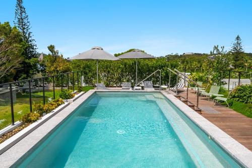 a swimming pool with chairs and umbrellas in a yard at Jonson Lane Apartments in Byron Bay