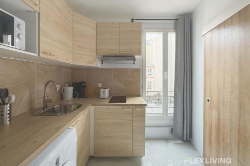 une cuisine avec des armoires en bois, un évier et une fenêtre dans l'établissement Flexliving - studio - Faubourg Saint-Antoine, à Paris