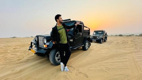 a man standing in front of a jeep in the desert at Arman Desert Luxury Camp & Resort Jaisalmer in Jaisalmer