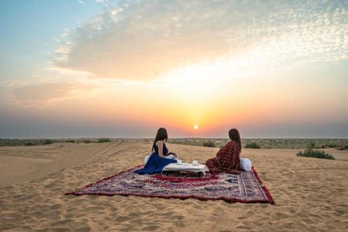 two women sitting on a blanket in the desert watching the sunset at Arman Desert Luxury Camp & Resort Jaisalmer in Jaisalmer