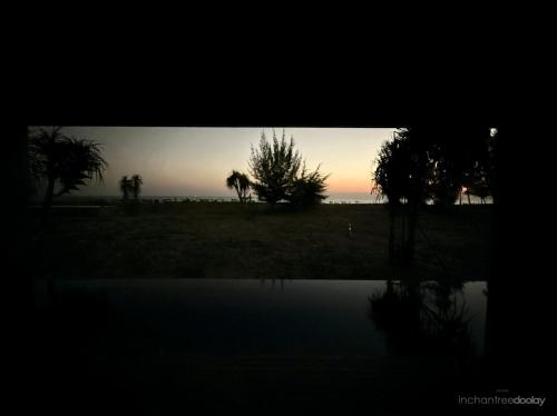 a sunset over a field with trees and a body of water at inchantreedoolay huahin in Pran Buri