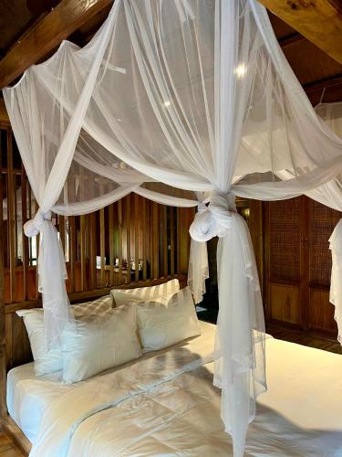 a bedroom with a canopy bed with white sheets and pillows at Hang Mua Ecolodge in Ninh Binh
