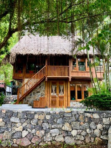 a house with a thatched roof and a stone wall at Hang Mua Ecolodge in Ninh Binh